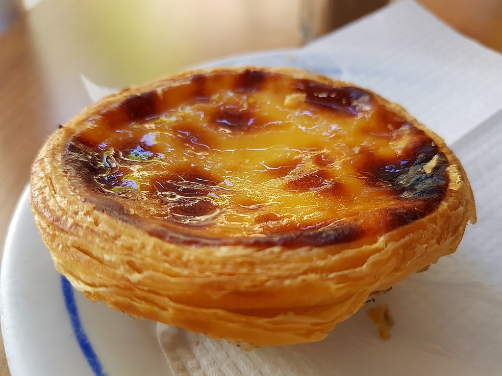 A plate with a small tart of flaky pastry and a creamy egg filling.