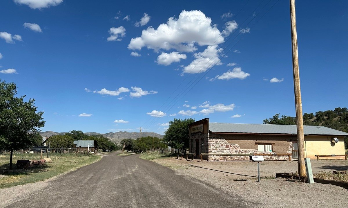 An empty street with one or two old buildings and mountains in the distance.